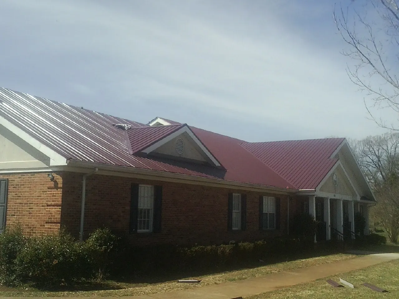 Red metal roof with gabled entries on a long brick building, from a Hail Damage Roof Repair job in Madisonville