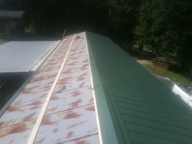 Old rusted panels beside newly installed green metal roofing — Wind Damage Roof Repair by Roofing Brothers in Madisonville