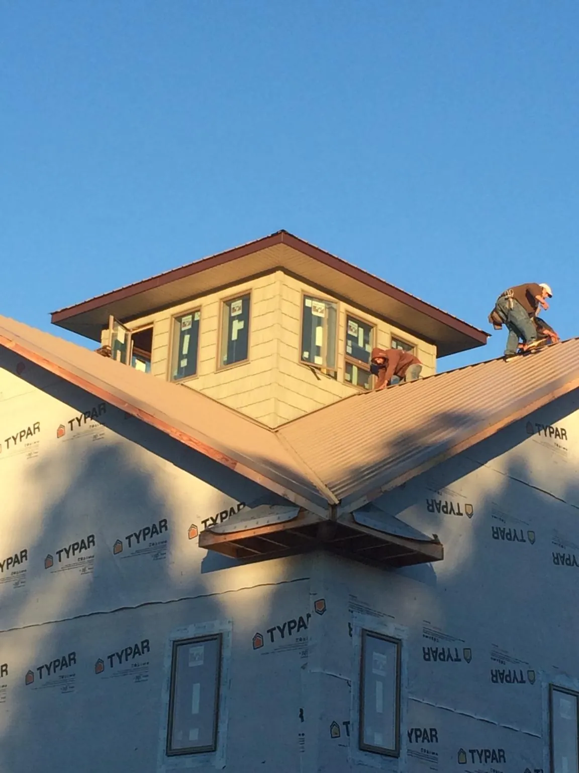 Roofers working around a rooftop cupola on a new metal roof at sunset — Roof Waterproofing in Madisonville by Roofing Brothers